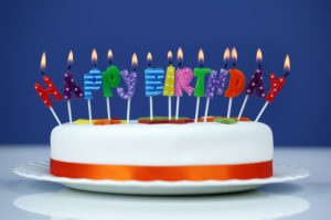 Happy birthday candles on a white cake over blue background