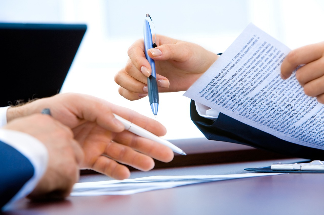 Two people's hands holding pens and paperwork.