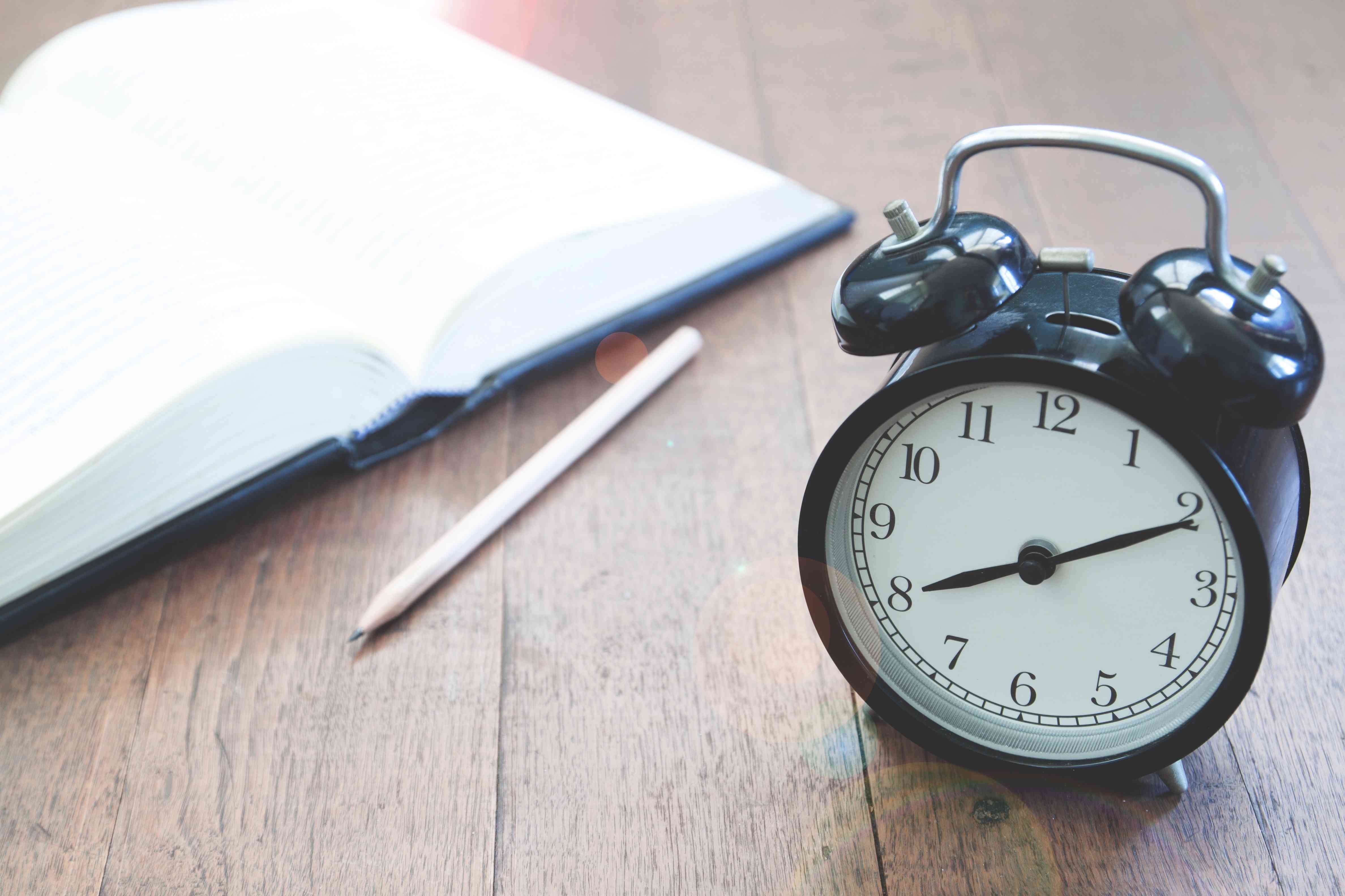 Alarm clock with notebook and pencil on a desk.